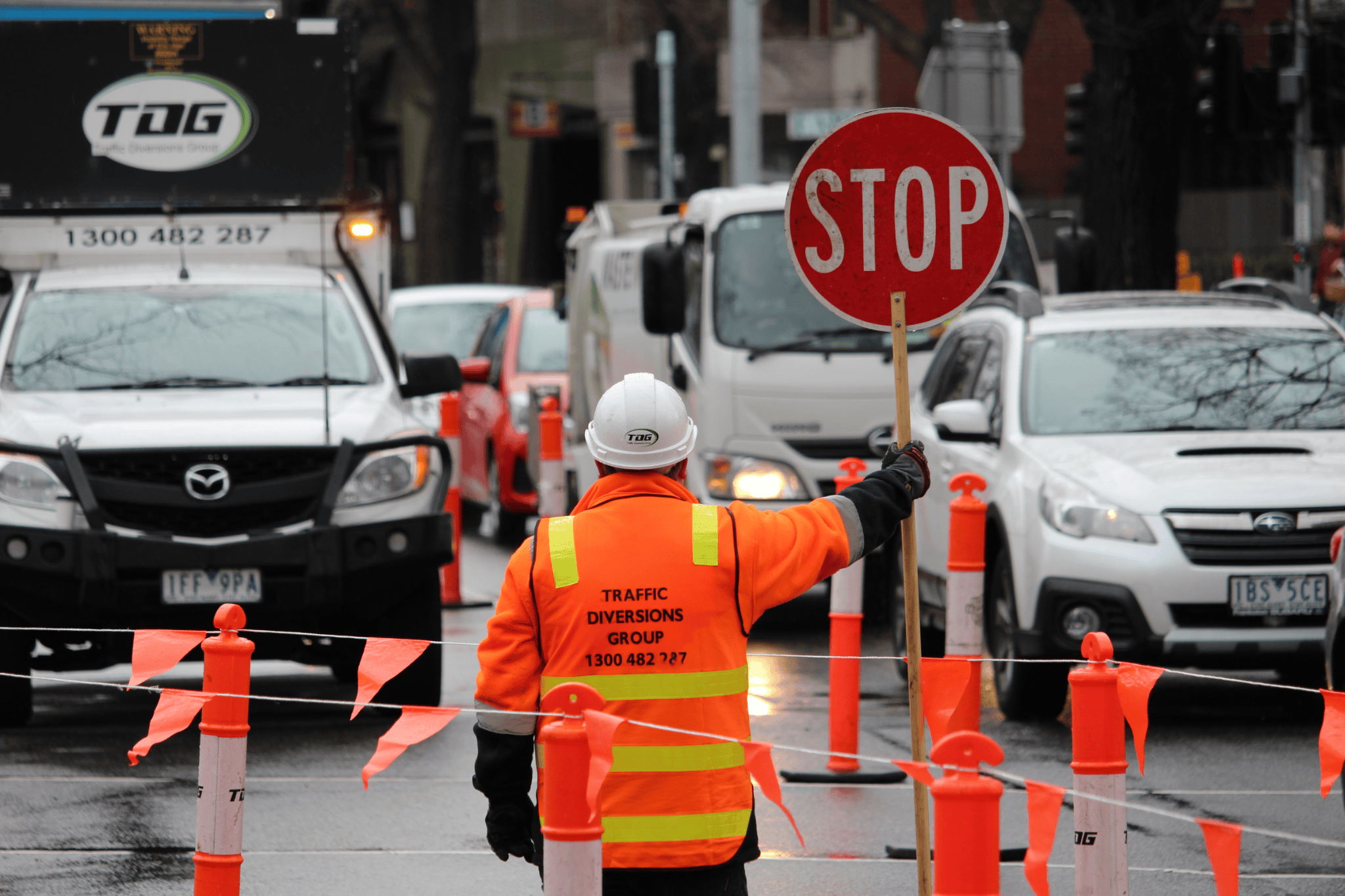 Traffic management team holding stop sign and directing traffic among cones and bunting.